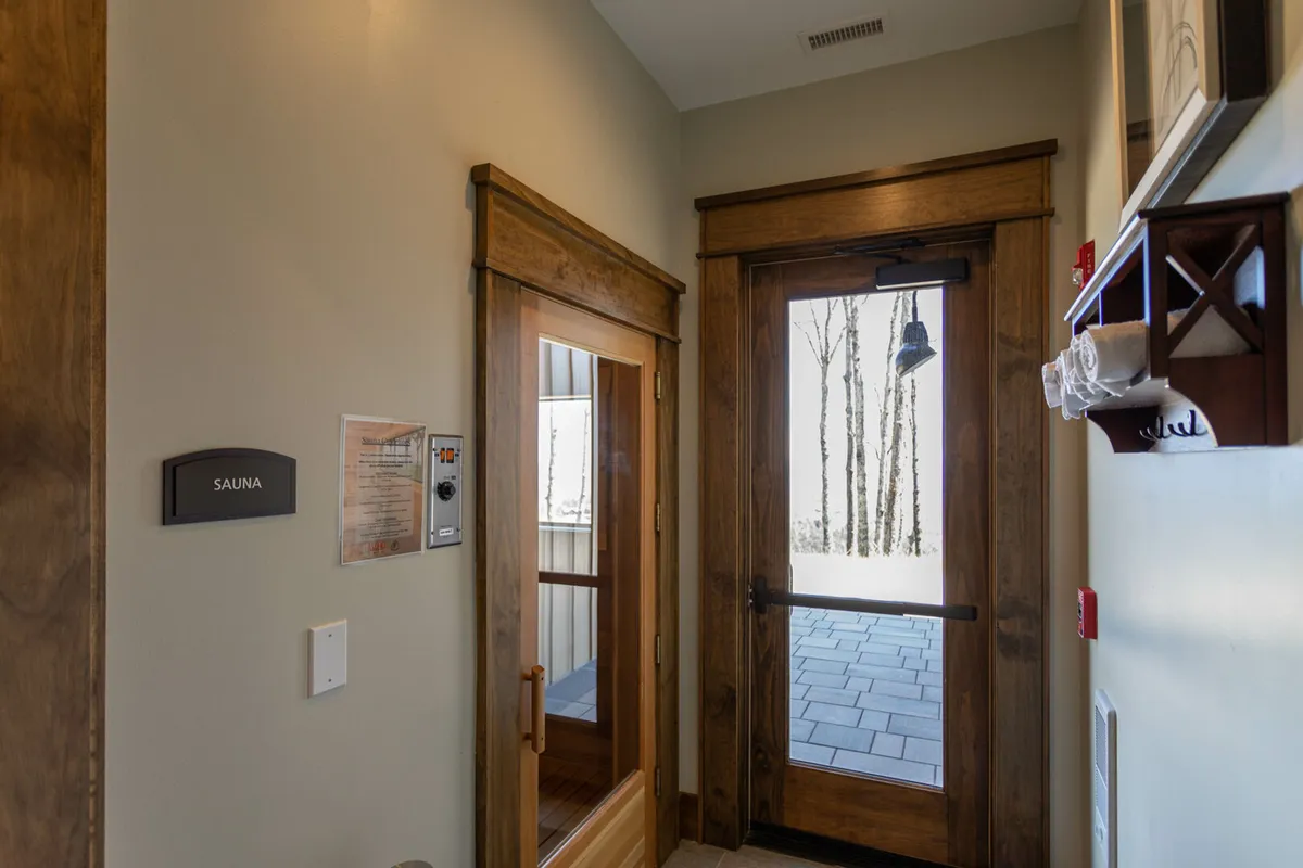 A serene interior featuring a wooden sauna door and warm wood accents, with a view to the outdoors through glass. The space exudes tranquility, inviting moments of relaxation and rejuvenation.