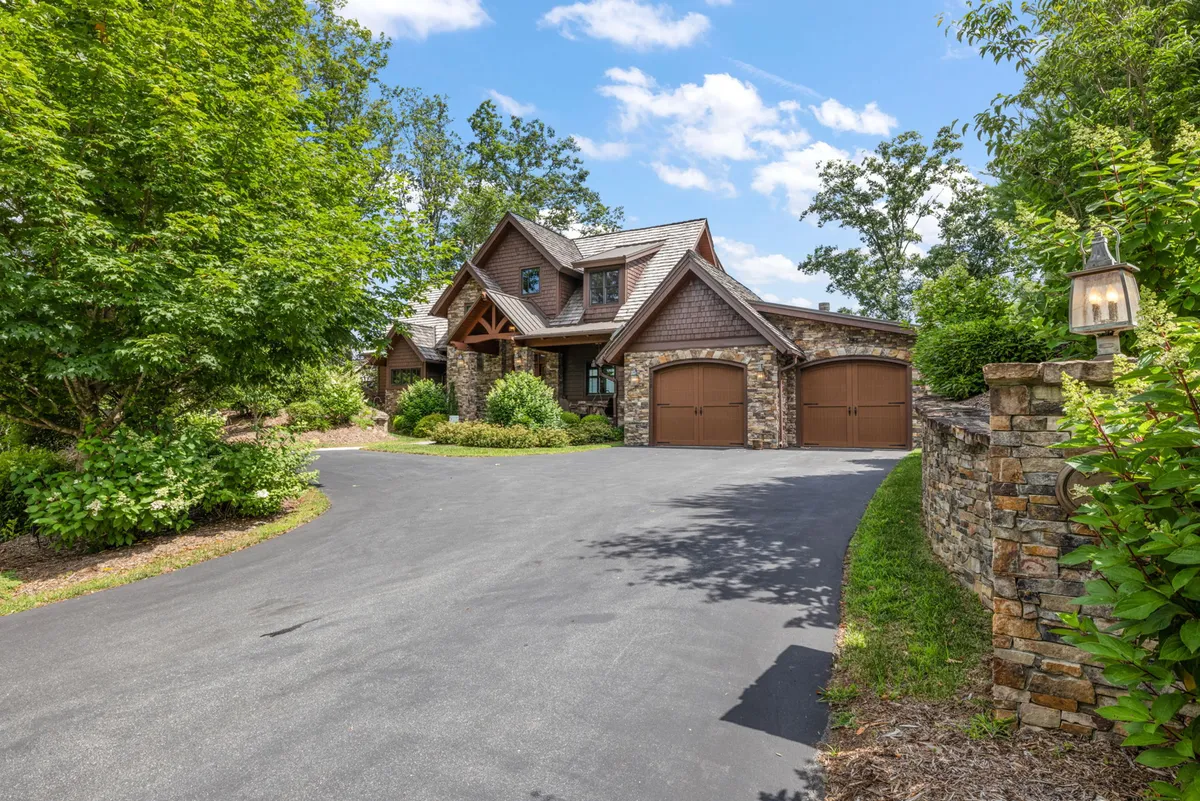 A view of the home’s stone facade and wooden garage doors, with a spacious front porch nestled among natural landscaping. The setting evokes warmth, privacy, and the comfort of a private residence within the community.