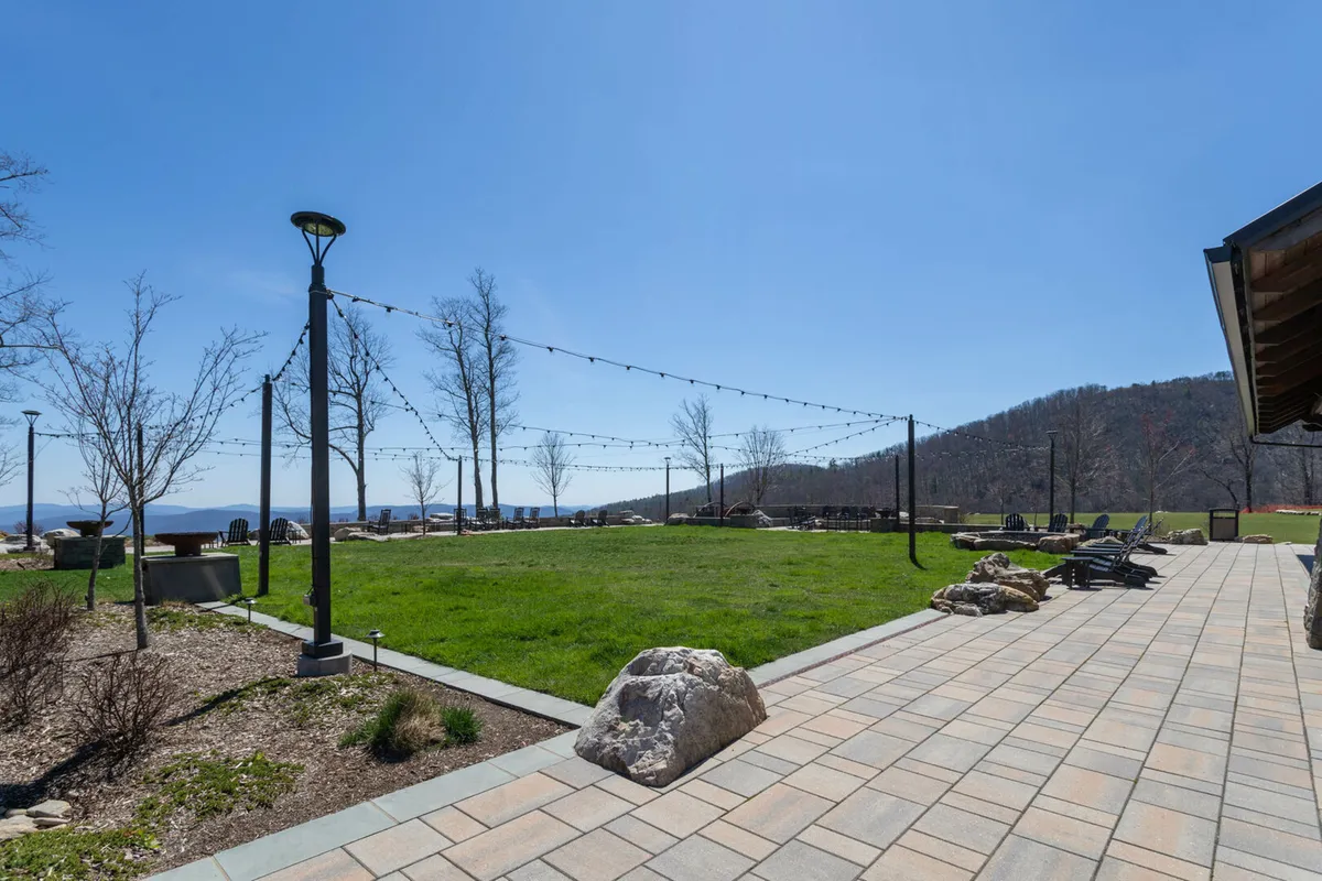 A cheerful outdoor gathering space with stone pathways, a lush lawn, ample seating, string lights, and a mesmerizing mountain backdrop. The scene is lively yet relaxed, ideal for picnics, stargazing, or socializing while soaking in mountain beauty.