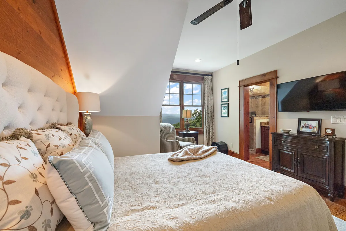 This image presents a stylish bedroom complete with a decorative headboard, a window with a scenic view, a dressing area with a chair, and a wall-mounted Smart TV. The thoughtful layout and modern amenities highlight the suite’s functionality and comfort.