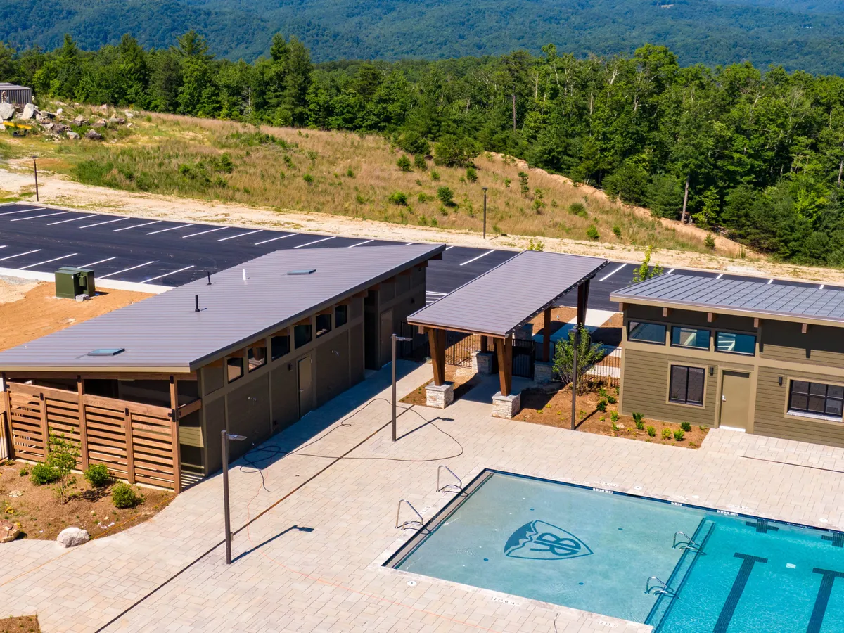 A vibrant exterior view of a swimming pool surrounded by landscaped areas and buildings. Guests can be seen swimming, relaxing by the pool, and engaging in social gatherings, with sunlit conditions and a communal mood.