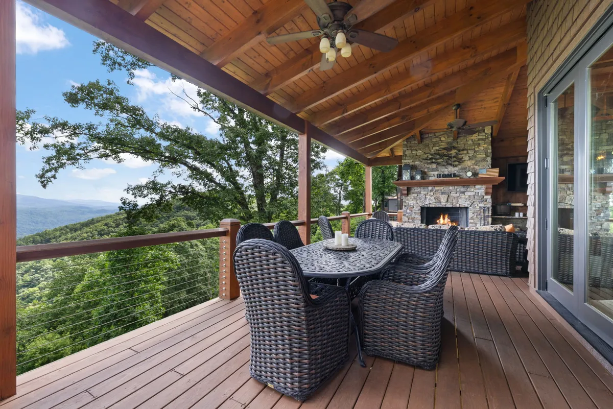 An inviting outdoor dining area with a stone fireplace and Adirondack chairs, set against a panoramic mountain view. The space is designed for social gatherings, fireside relaxation, and intimate meals beneath an open sky, especially during sunset or starlit evenings.