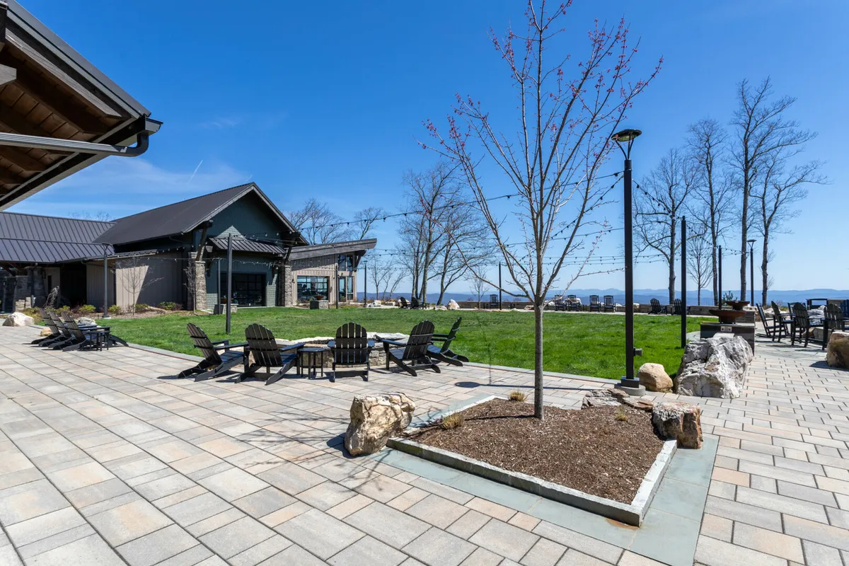 A welcoming outdoor seating area with Adirondack chairs arranged for conversation, lush landscaping, and a modern building in the background. The area is set up for relaxation, group gatherings, or shared outdoor dining, with a pathway leading through the community and scenic sunset views.