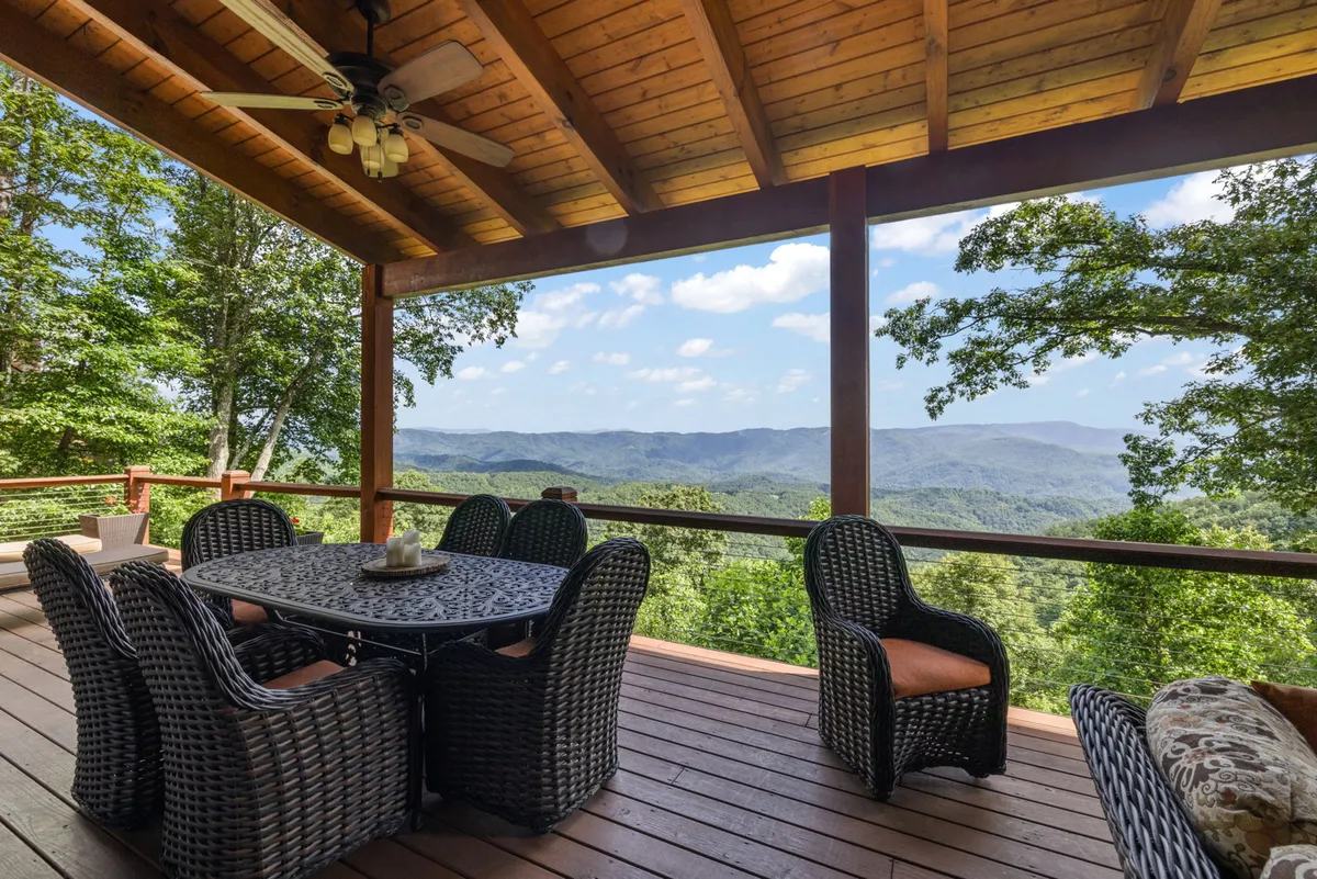 This image captures an outdoor dining table with woven chairs set under a wooden ceiling, offering panoramic mountain views. The space is serene and perfectly suited for both sunrise breakfasts and stargazing at night, with the robust design evoking warmth and comfort for gatherings.