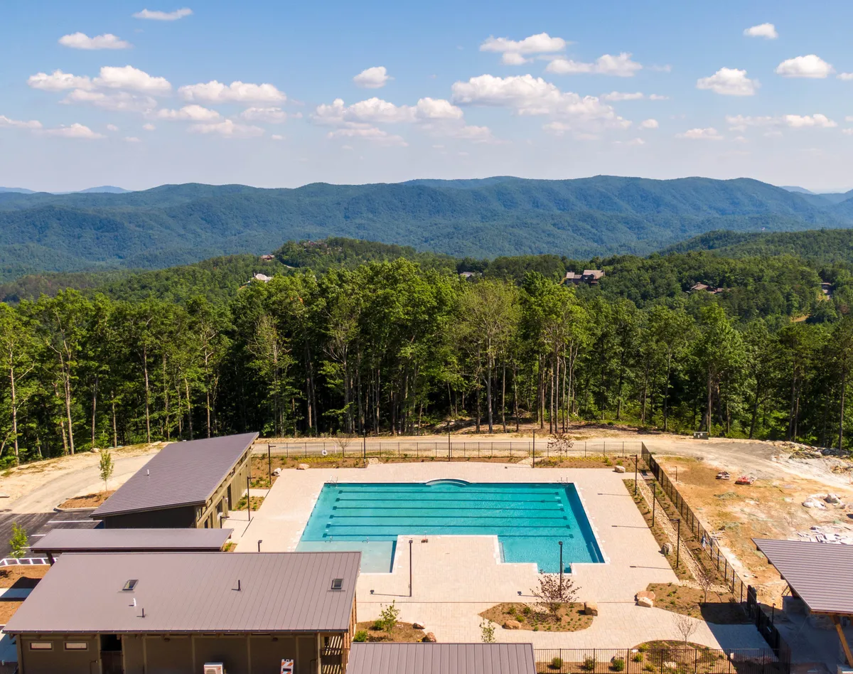A modern, resort-style swimming pool set against a breathtaking mountain backdrop, surrounded by trees and contemporary buildings. The scene is tranquil and inviting, with ample space for sunbathing, socializing, and enjoying communal amenities.